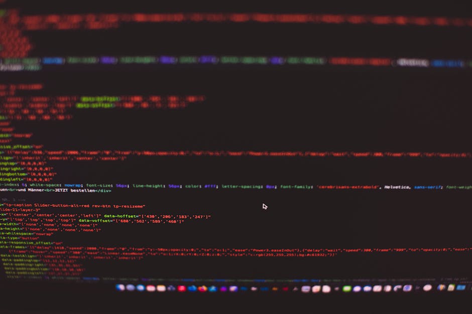 A close-up of a computer screen displaying lines of colorful code in red, green, blue, and purple on a dark background, indicative of programming or web development. The code appears organized with sy